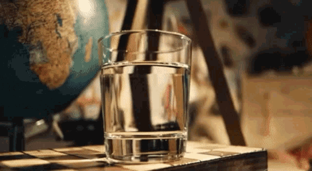 a glass of water is sitting on top of a chess board next to a globe .
