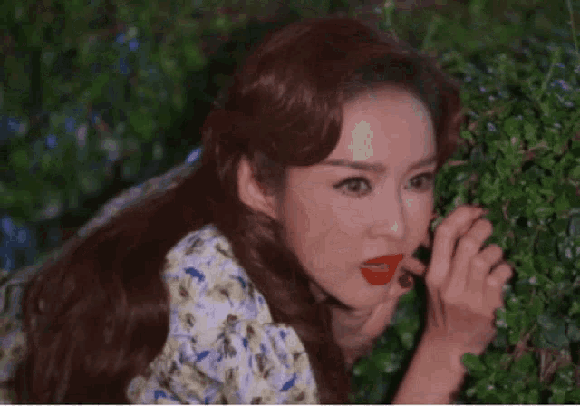 a woman with red lipstick is peeking out from behind a bush ..