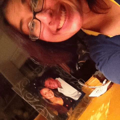 a woman wearing glasses smiles in front of a picture of a man and a woman