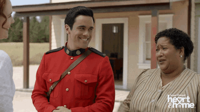 a man in a red uniform is smiling while talking to a woman in front of a house that says heart on me