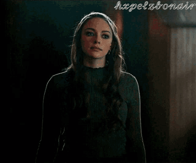 a woman in a green sweater is standing in the dark
