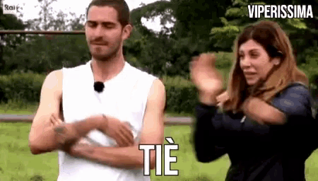 a man in a white tank top is standing next to a woman who is clapping her hands in a field .
