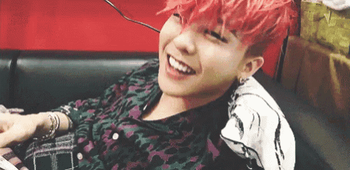 a young man with pink hair is sitting on a couch smiling .