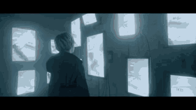 a man is standing in front of a wall filled with lots of screens .