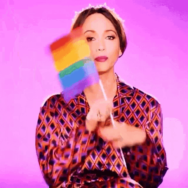 a woman in a plaid shirt is holding a rainbow flag in her hand .