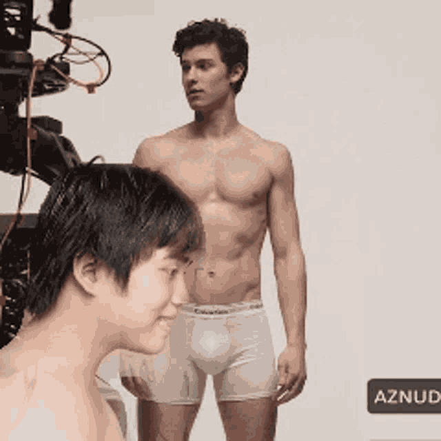 a shirtless man in calvin klein underwear stands next to a shirtless boy