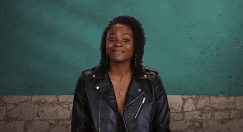 a woman wearing a black leather jacket smiles in front of a green wall