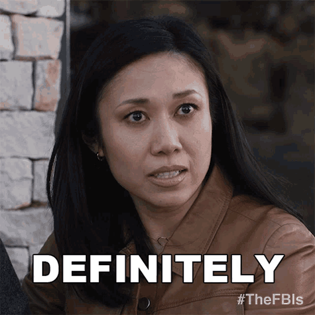 a woman in a brown jacket says " definitely " in front of a stone wall