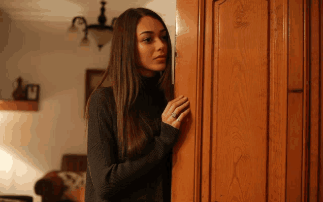 a woman in a black sweater is peeking out from behind a door