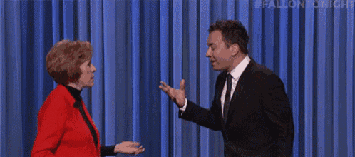 a man in a suit and tie is shaking hands with a woman in a red jacket .
