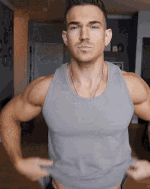 a man wearing a grey tank top is standing in a room with his hands on his hips