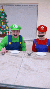 two men dressed as mario and luigi are sitting at a table with plates and spoons