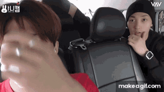 a man in a red shirt is sitting in the back seat of a car next to another man in a black hat