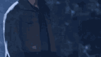 a man in a hooded jacket is standing in the dark in a foggy room .