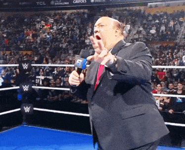 a man in a suit is holding a microphone in front of a wrestling ring