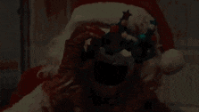 a person dressed as santa claus with a bloody face is holding a christmas ornament .