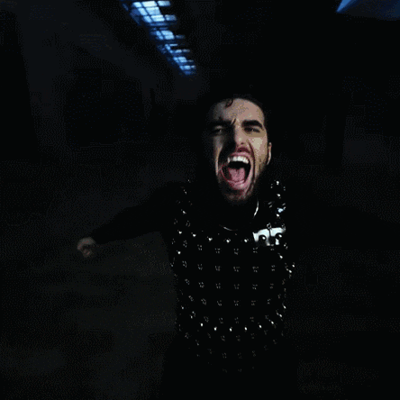 a man wearing a black vest with studs on it screams in a hallway
