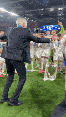 a man in a suit is dancing on a soccer field with a trophy in the background
