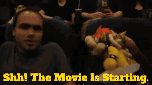 a man and a stuffed animal are sitting in a movie theater with the words shh the movie is starting behind them