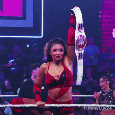 a woman in a red and black outfit is holding a wrestling belt in the air