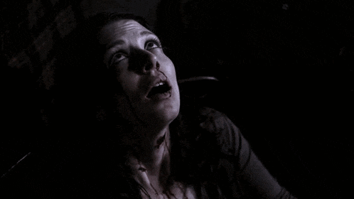 a woman with blood on her face is screaming in the dark with her mouth wide open .
