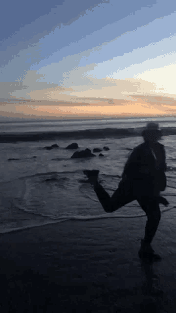 a person in a cowboy hat is running on the beach at sunset