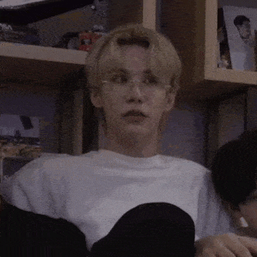 a man wearing glasses is sitting in front of a bookshelf .