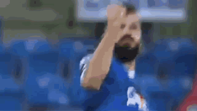 a soccer player in a blue shirt is talking to another player in a blue stadium .