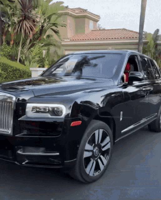 a black rolls royce is parked in front of a house with palm trees