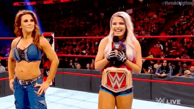 two women are standing in a wrestling ring and one is wearing a wwe championship belt