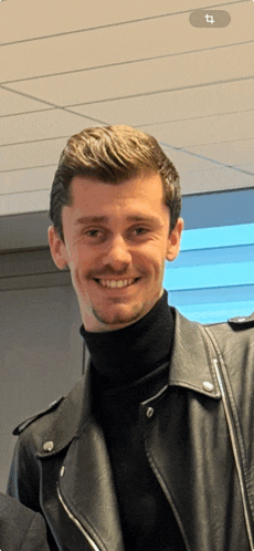 a man wearing a black turtleneck and a black leather jacket smiles for the camera