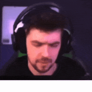 a man with a beard wearing headphones is sitting in front of a computer screen .