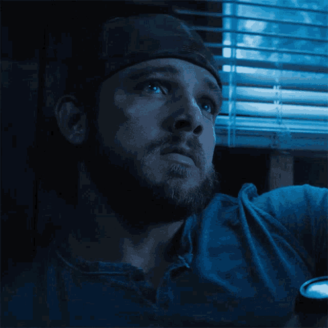 a man with a beard is looking out of a window with blinds
