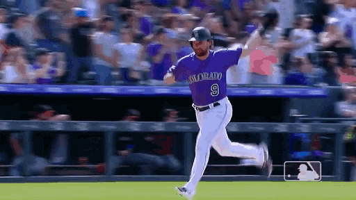 a baseball player wearing a purple colorado jersey is running on the field .
