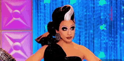 a drag queen is standing in front of a blue curtain wearing a black dress and white hair .