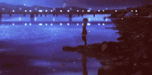 a girl is standing on the shore of a river at night