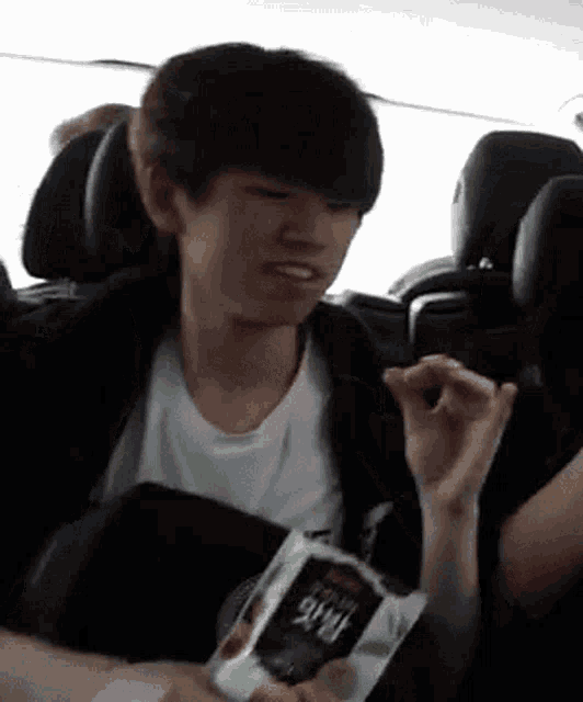 a young boy is sitting in a car eating a bag of chips .