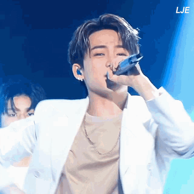 a man in a white jacket is singing into a microphone with the letters lje in the background