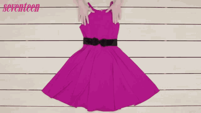 a purple dress with a black belt and a pair of black shoes on a wooden surface