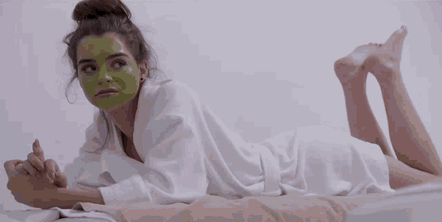a woman with a green mask on her face laying on a bed