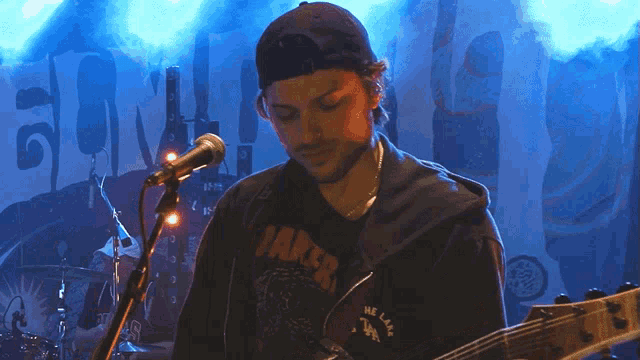 a man is playing a guitar and singing into a microphone while wearing a shirt that says " the lake "