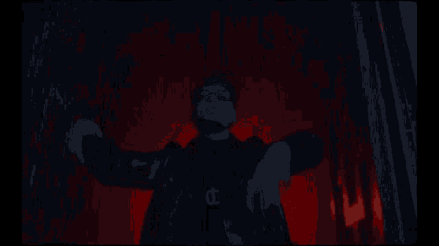 a man with his arms outstretched in a dark room with a red light behind him