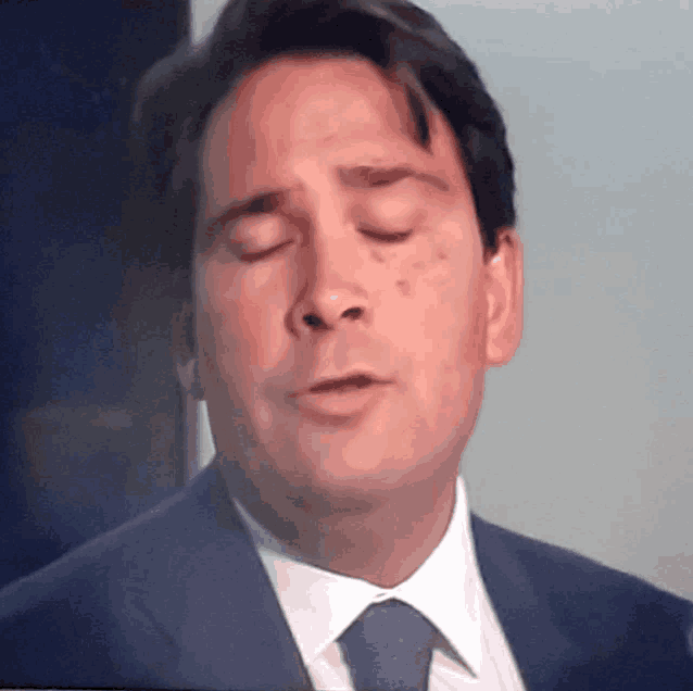a man in a suit and tie is making a funny face with his eyes closed