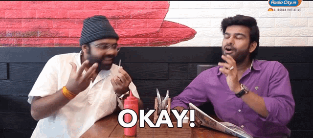 two men sitting at a table with the word okay on the table