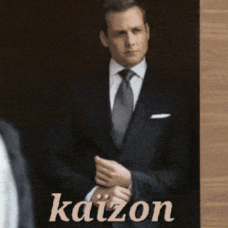 a man in a suit and tie is standing in front of a wall that says kaizon