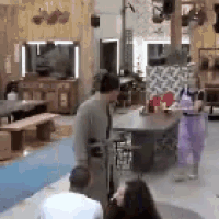 a group of people are standing in a room with a table and benches .