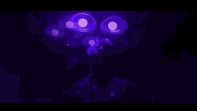 a man is standing in a dark room with purple lights behind him