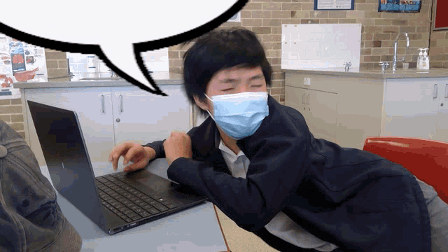a man wearing a mask sits at a desk with a laptop