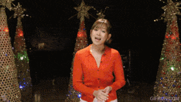 a woman in a red shirt is standing in front of christmas trees with gifrun.com in the corner