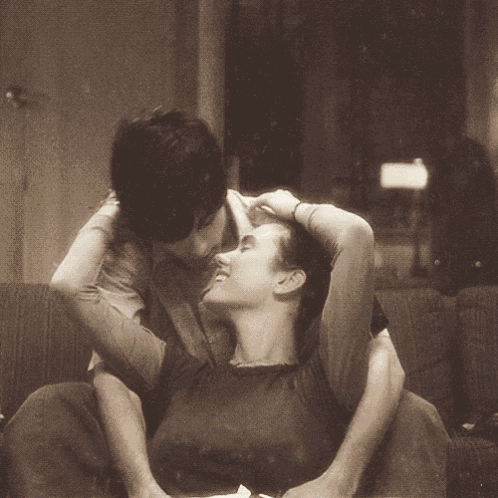 a man and woman kissing on a couch with their arms around each other